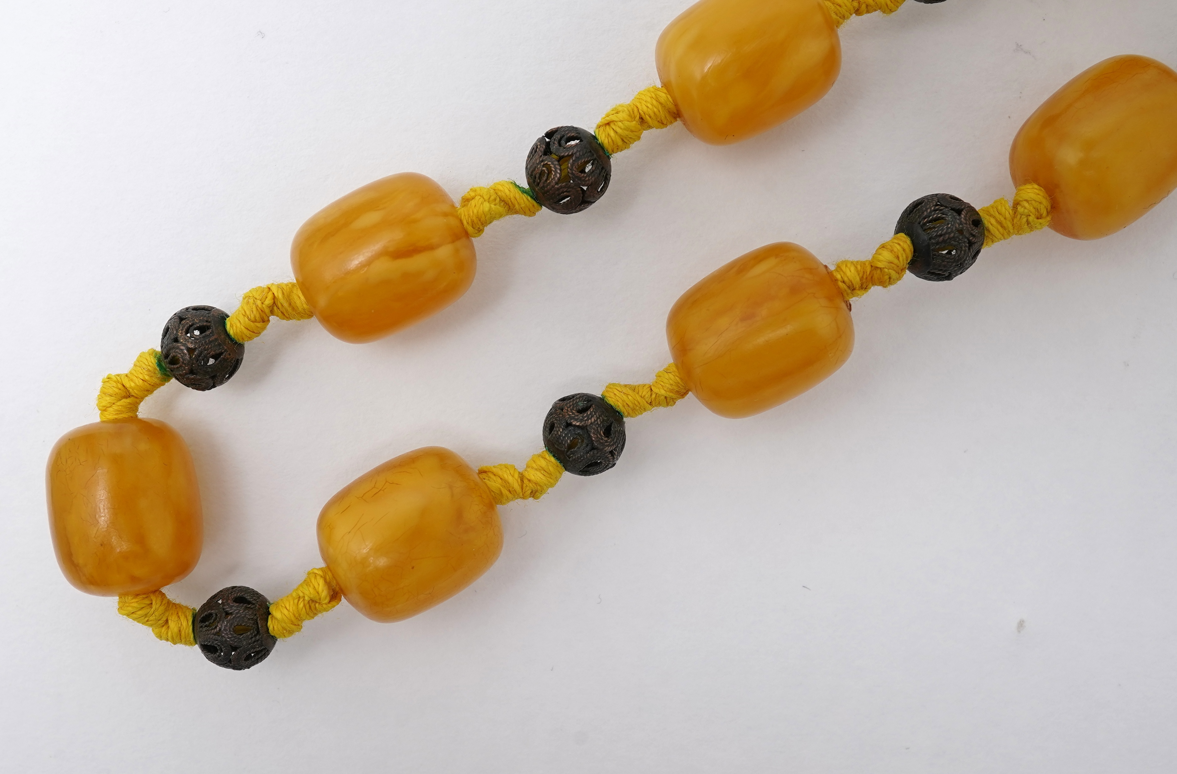 An amber necklace and carving, comprising: an amber necklace, composed of beads each measuring approximately 12 x 12 x 14mm, spaced by openwork metal beads, length 48cm; and an amber carving of a hawk on a rock, length 4